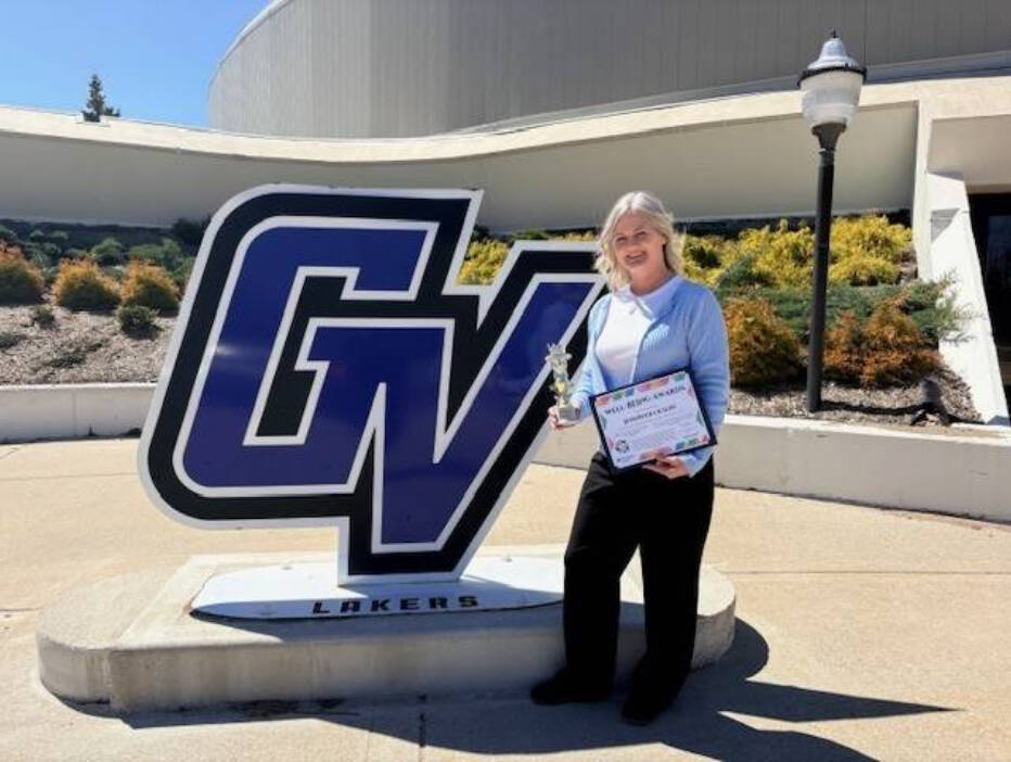 Jen Olson posing in front of GVSU Sign with her Golden Apple Award